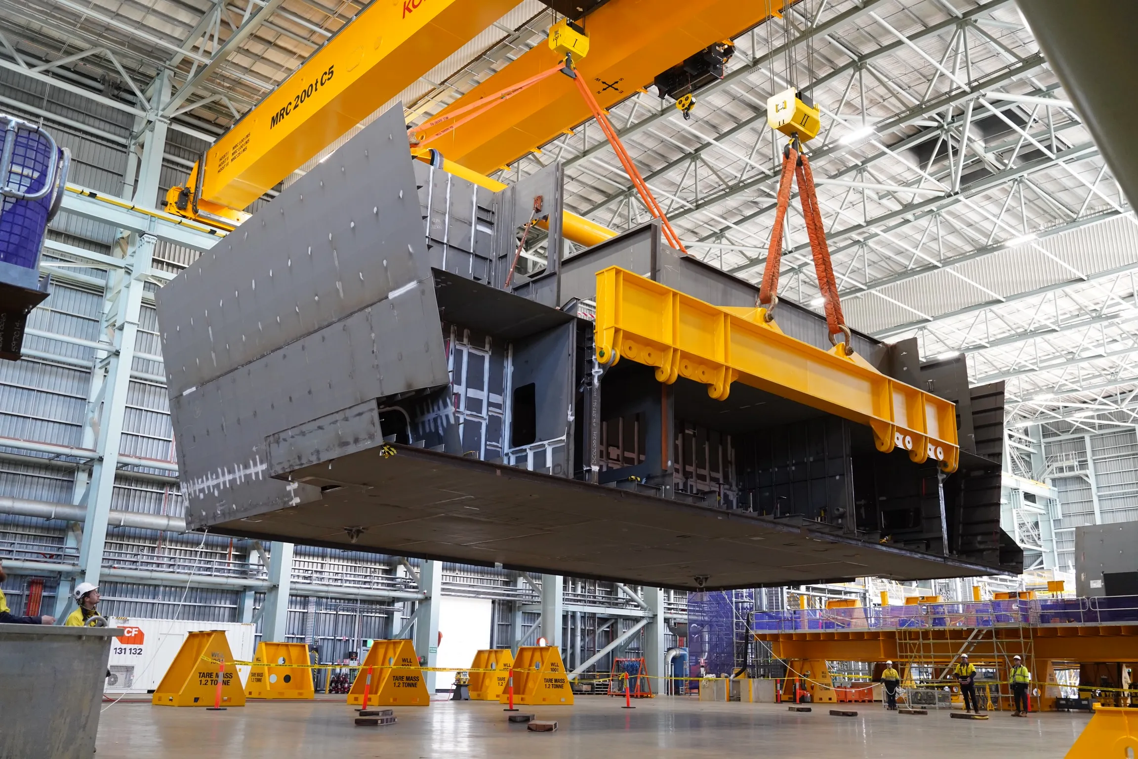 Ship block being hoisted onto a lifting beam in the construction hall